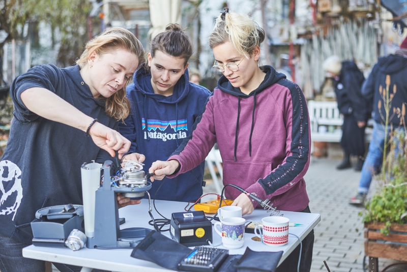 Drei Personen stehen vor einem Tisch und reparieren ein kaputtes Gerät