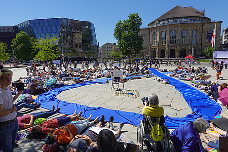Liegend-Demonstration auf dem Platz der Alten Synagoge. In der Mitte liegt eine blaue Stoffschleife mit 10m Länge.
